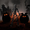 A full-body plastic skeleton figurine stands between two carved jack-o'-lanterns in a dark, spooky setting.