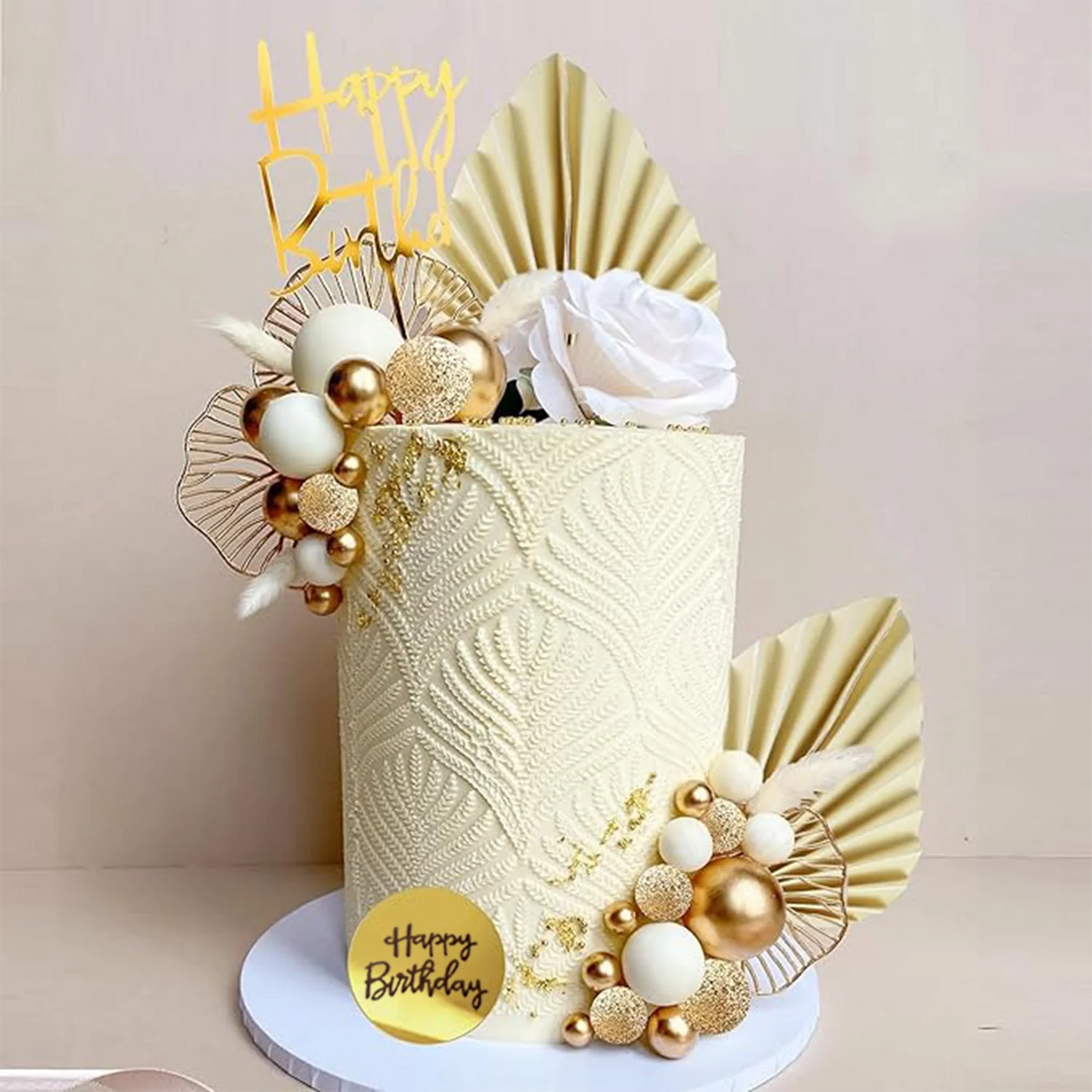 A tiered cake decorated with white, gold, and beige elements including floral accents and fan shapes.