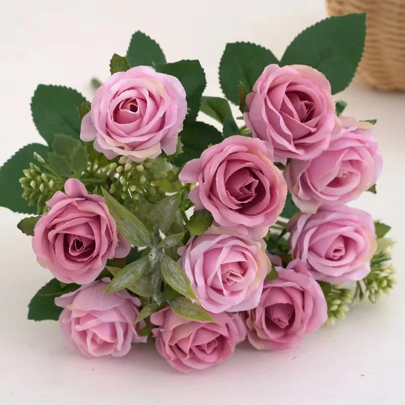 A bouquet of artificial pink and mauve roses with green leaves and small filler flowers.