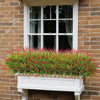A vibrant green and red artificial lavender wreath in a white planter box mounted on a brick wall.