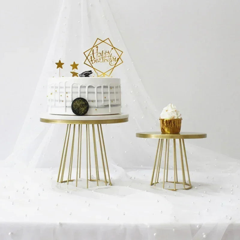 Ein mehrstöckiges weißes Kuchen mit goldenen Akzenten steht auf einem goldenen Metallständer neben einer weiteren kleinen gol