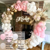 A balloon garland arch kit featuring pink and beige balloons decorating a brick fireplace mantel.