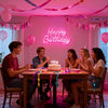 A group of friends celebrating a birthday with a neon sign that reads Happy Birthday
