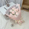 A bouquet of pink and white artificial roses wrapped in light pink paper sits on a white surface.