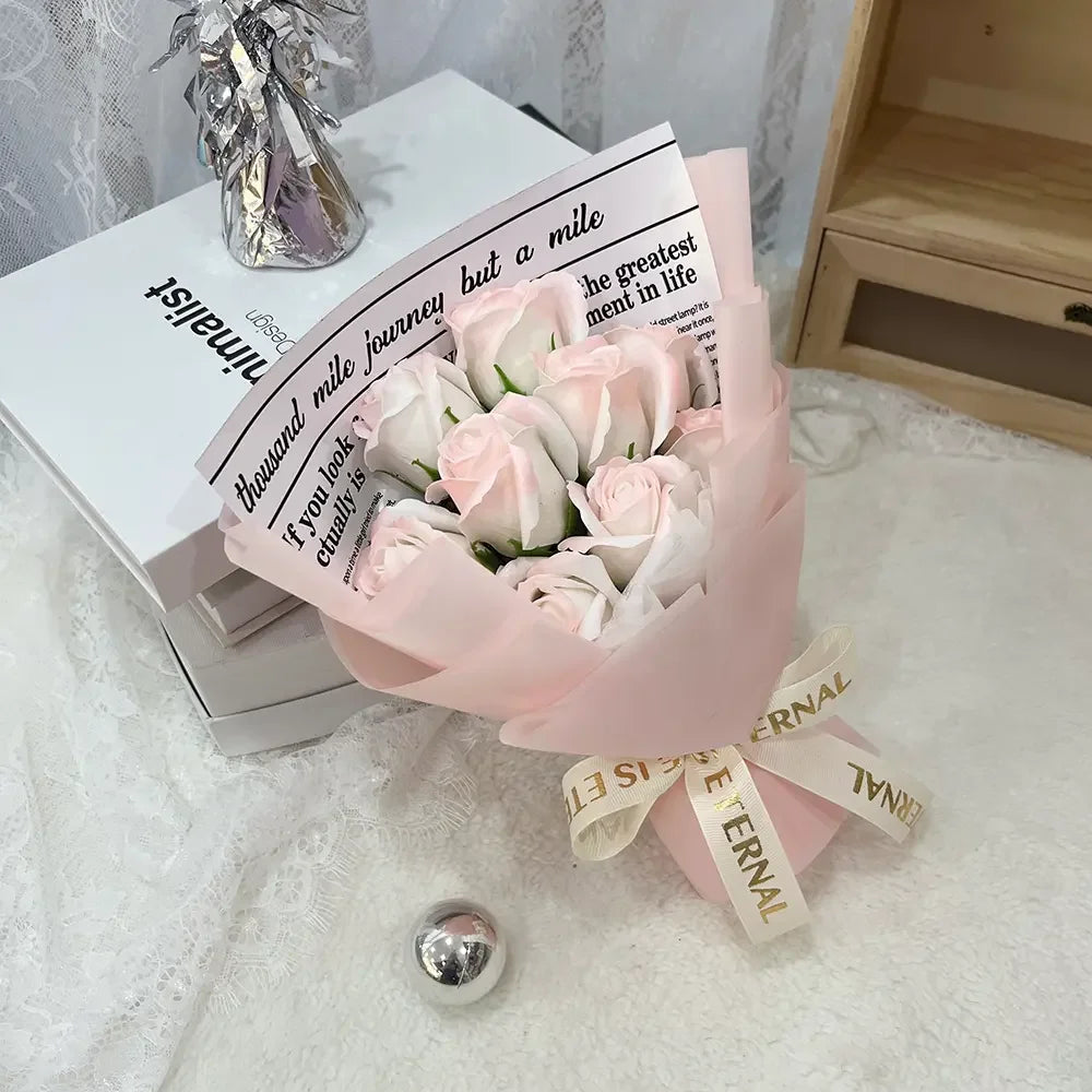 A bouquet of pink and white artificial roses wrapped in light pink paper sits on a white surface.