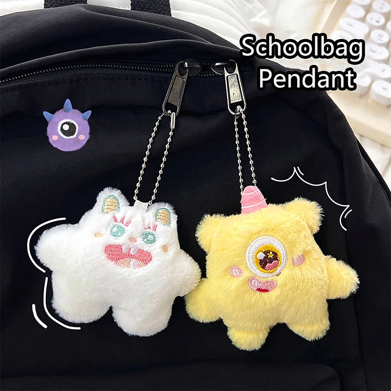 A white fuzzy plush monster pendant with pink accents is attached to a black schoolbag.
