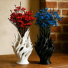 A pair of modern plastic flower vases, one white and one black, holding vibrant red and blue flowers against a brick backgrou