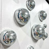 Silver disco balls are mounted on a white wall, creating a sparkling decorative display.