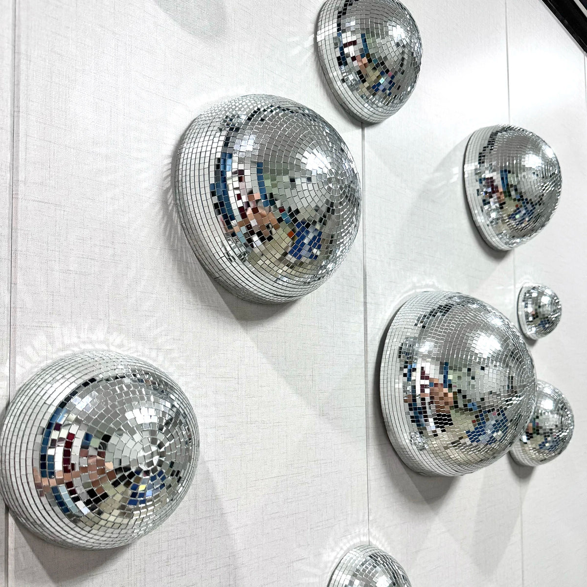 Silver disco balls are mounted on a white wall, creating a sparkling decorative display.