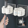 A hand is installing an adhesive wall hook for mops and brushes onto a vertical pole.