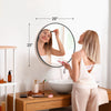 A woman is looking in a large round vanity mirror with a matte metal frame.