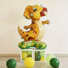 A yellow and orange foil animal balloon shaped like a dinosaur stands on a green leaf base with several loose balloons.