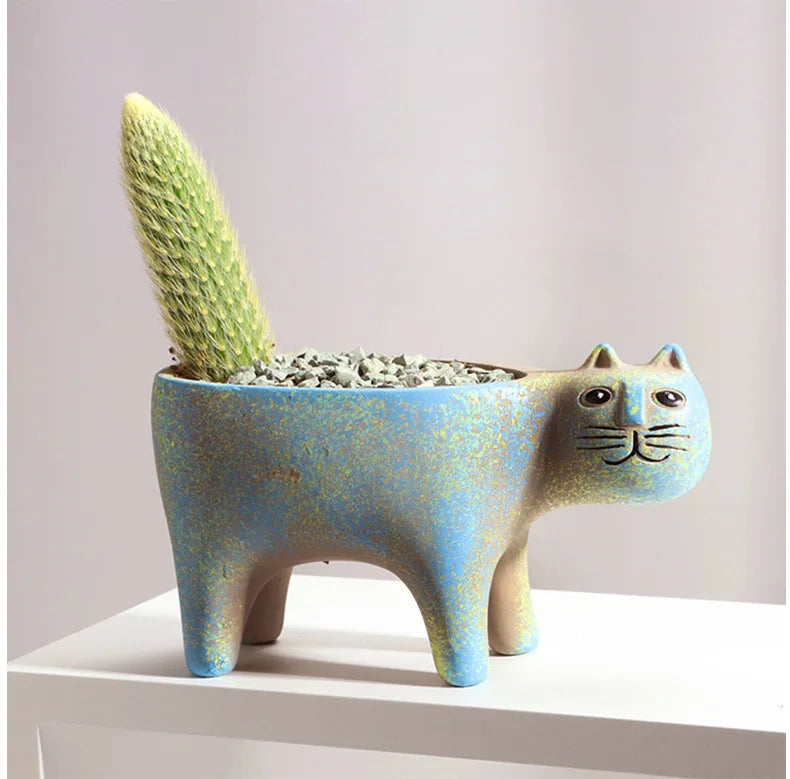 A ceramic planter shaped like a cat holding a green succulent plant.