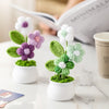 Hand woven crochet flowers in white and purple are potted in small white ceramic cups on a marble surface.