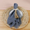 A folded gray cotton napkin with a tasseled tie rests on a round woven mat.