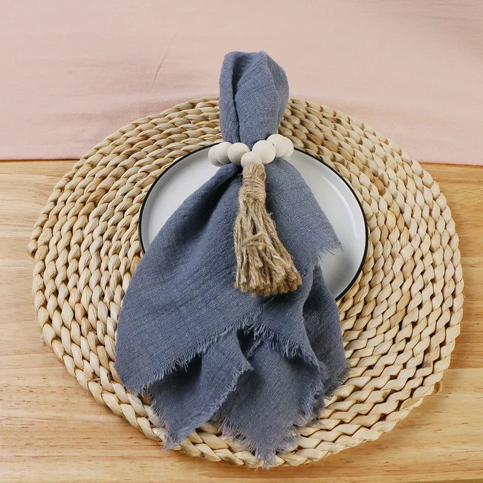 A folded gray cotton napkin with a tasseled tie rests on a round woven mat.