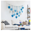 Bohemian macrame leaf wall hanging with blue and beige tassels displayed on a white wall above a sofa.