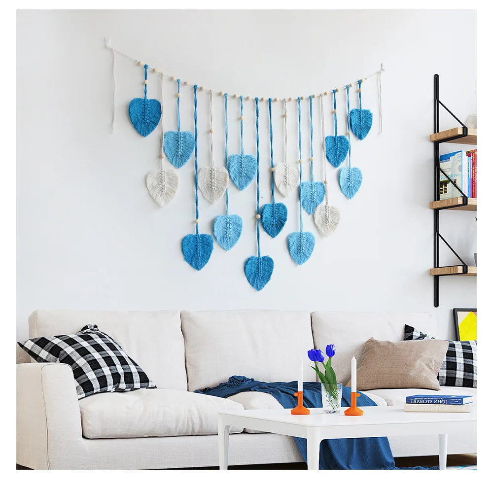 Bohemian macrame leaf wall hanging with blue and beige tassels displayed on a white wall above a sofa.