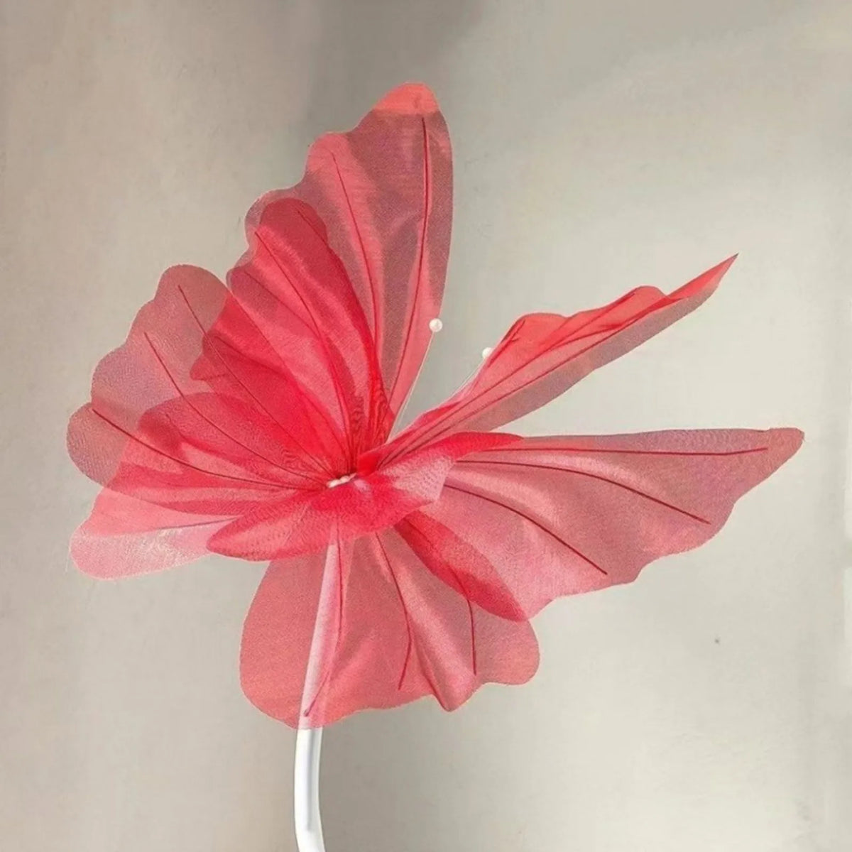 A vibrant pink and red sheer fabric butterfly decoration mounted on a white stick.