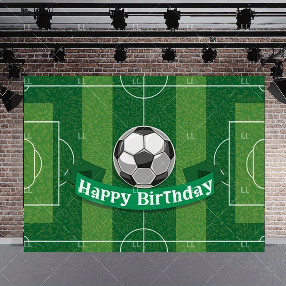 A green soccer field backdrop featuring a soccer ball and a Happy Birthday banner on a brick wall.