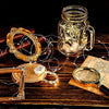 A glass jar filled with fairy lights and a gold wire wreath are displayed on a wooden surface.