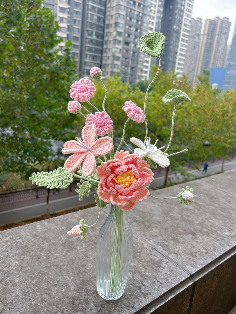 Un ramo de flores de ganchillo hecho a mano en tonos rosa y verde, exhibidas en un jarrón de vidrio.