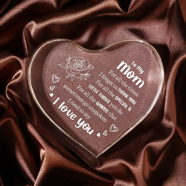 A clear acrylic heart pendant engraved with 'I love you' and a rose design, resting on dark brown satin fabric.