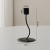 A black iron candle holder with a slender curved stem and a round base, shown against a light background.