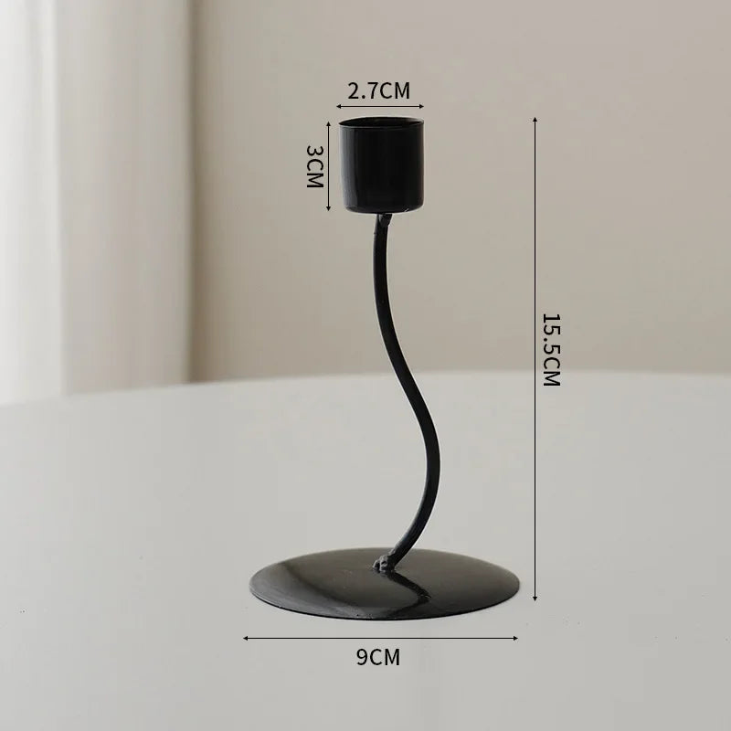 A black iron candle holder with a slender curved stem and a round base, shown against a light background.