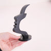 A black minimalist side face glasses holder shaped like a stylized profile, held by a hand.