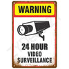 A vintage warning sign with a yellow banner and black graphic indicating 24 hour video surveillance.