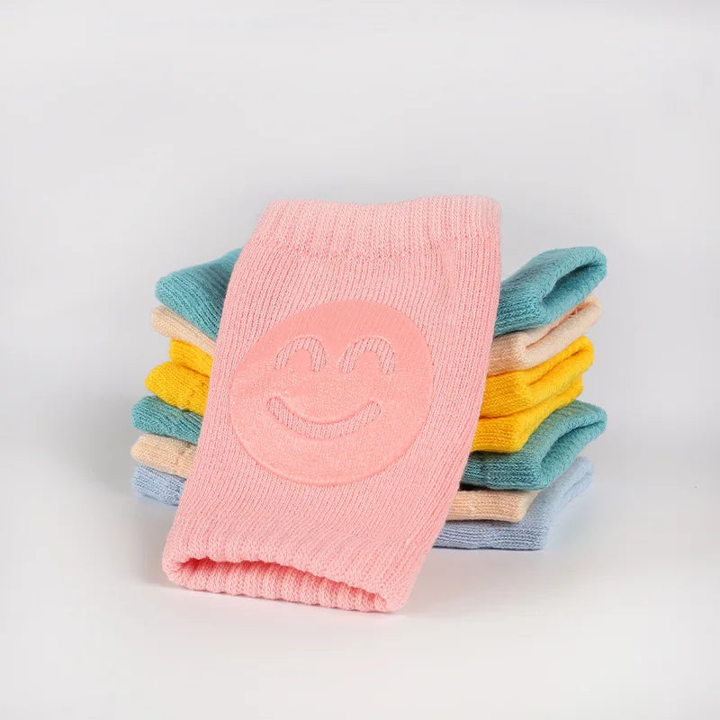 A stack of pink knitted knee pads with a smiling face in various pastel colors.