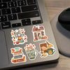 A laptop keyboard features several autumn-themed stickers including a house, books, and a mug.