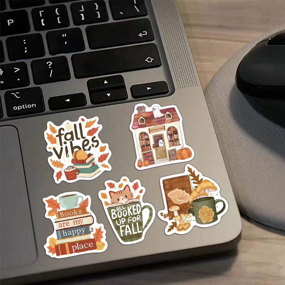 A laptop keyboard features several autumn-themed stickers including a house, books, and a mug.