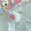 A small pink sausage-mouth plush charm with white eyes and a silver chain is resting on white tissue paper.