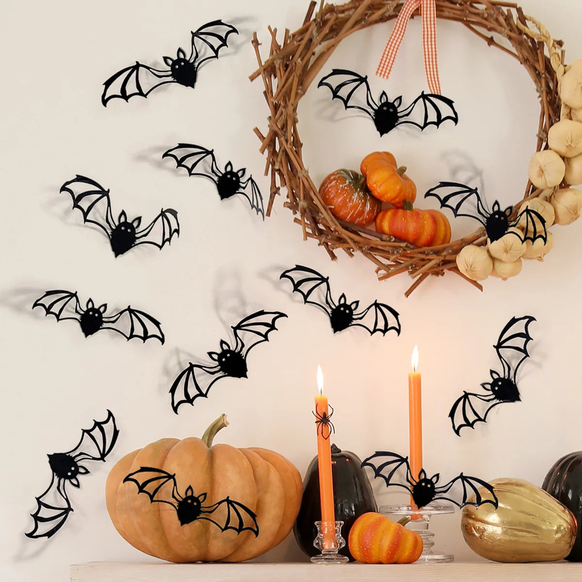 A decorative wreath of twigs surrounds black bat decals and pumpkins on a white wall.