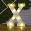 A glowing warm white LED alphabet letter light shaped like the letter X resting on a wooden surface.