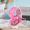 A pink glitter birthday candle shaped like the number 8 with a pink bow on a white stand.