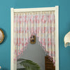 A white door frame decorated with a sheer pink lace curtain featuring floral embroidery and dangling tassels.