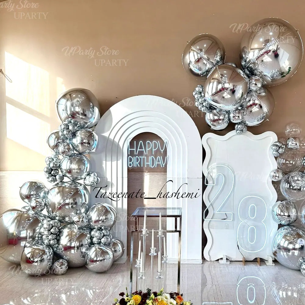 A display featuring metallic silver foil balloons arranged in a tree shape and clustered groupings against a white arch backd