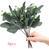 Five artificial eucalyptus stems with green leaves and small white flowers held in a hand.