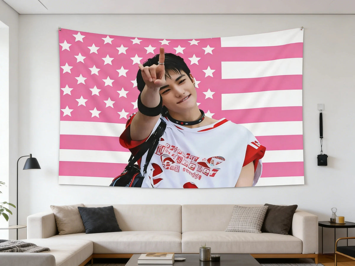 A portrait of Hyunjin making a finger sign against a pink American flag tapestry.