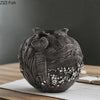 A dark gray resin vase with intricate swirling patterns sits on a wooden surface.