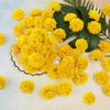 A bunch of bright yellow silk marigold flowers arranged on a white surface with green leaves.