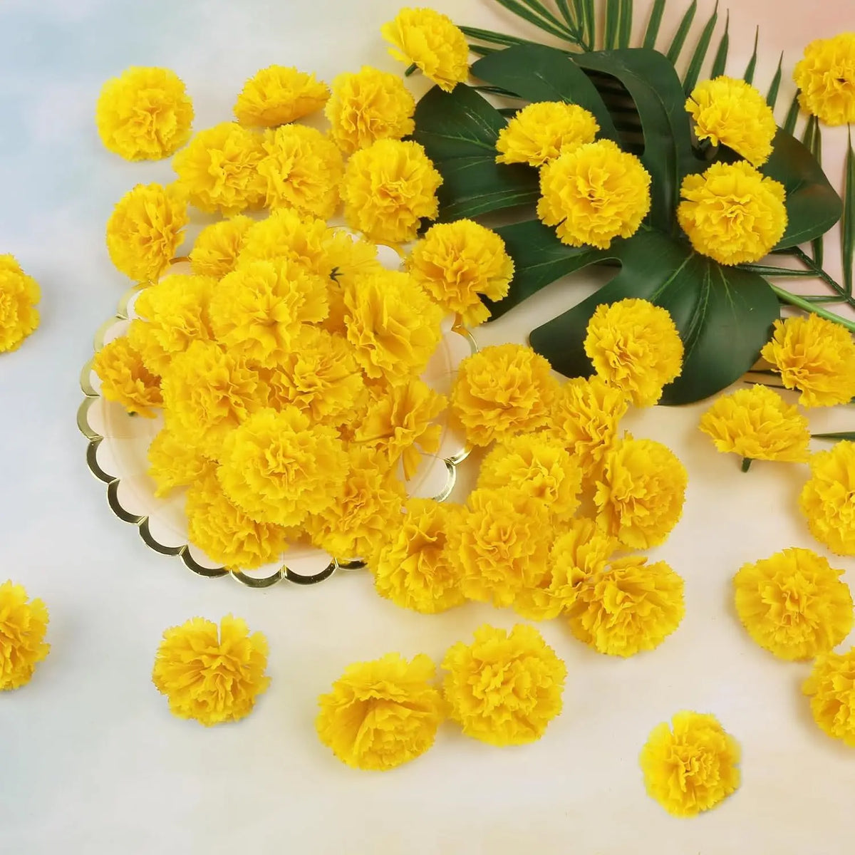 A bunch of bright yellow silk marigold flowers arranged on a white surface with green leaves.