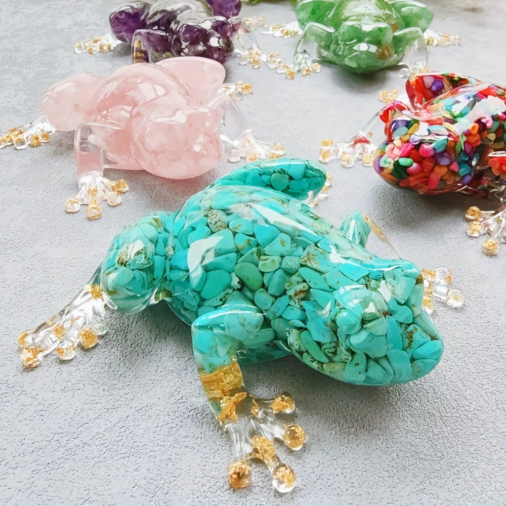 A vibrant turquoise crystal frog resin craft decoration surrounded by various colored crystals on a gray surface.