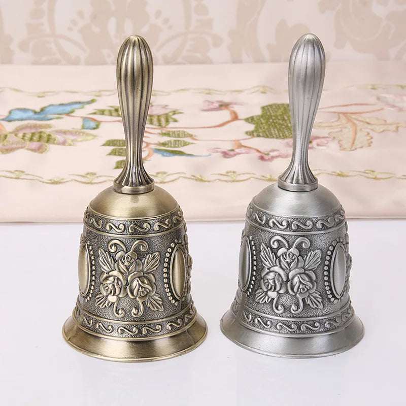 Ornate brass hand call bell with a decorative floral design and a silver-toned finish.