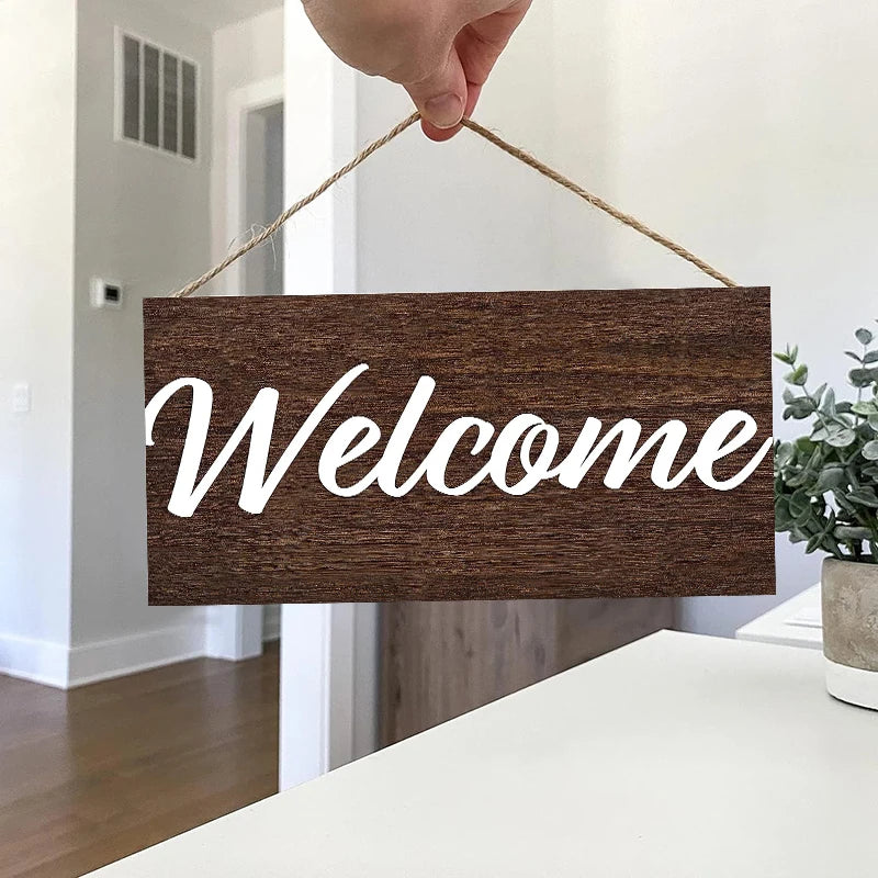 A rustic wooden welcome sign with white script 'Welcome' is being held by a hand, displayed on a white surface.