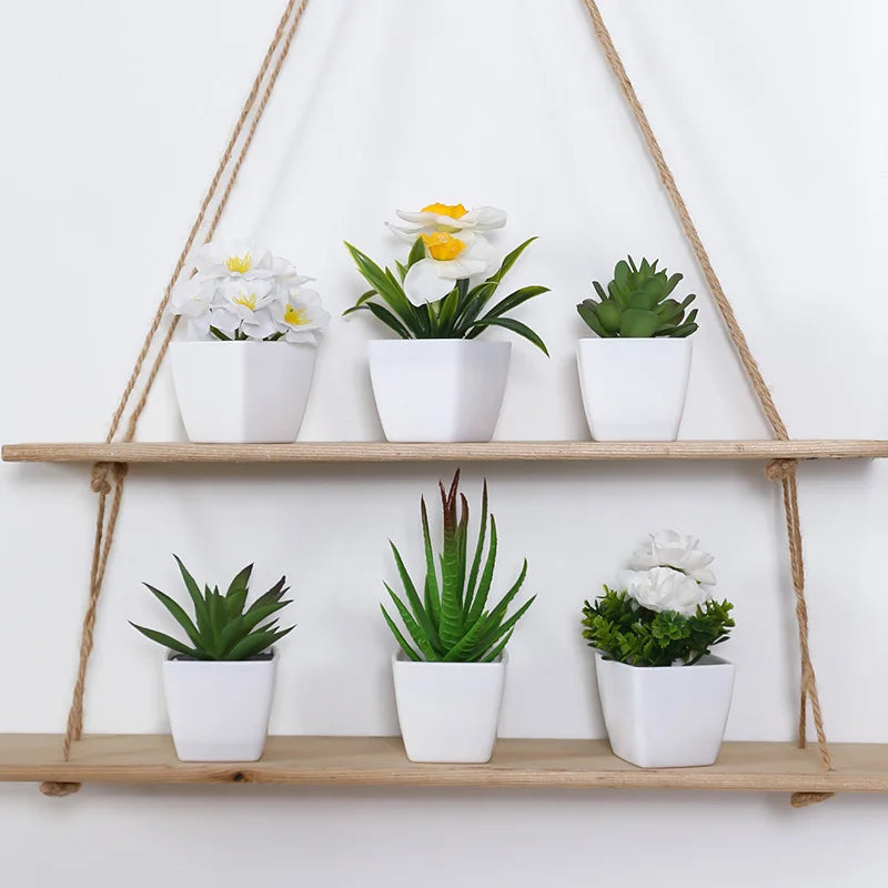 A display of six white artificial flowers and succulents in individual white pots hanging from a wooden shelf.