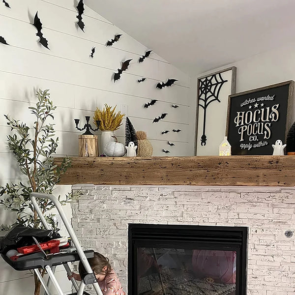 A shelf display featuring black PVC bat wall decorations and Halloween decor above a white brick fireplace.